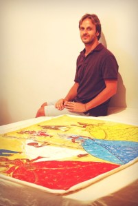 Dionisis sits by a colourful painting of various Orishas